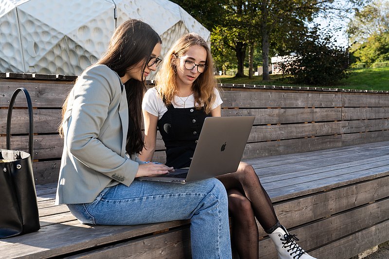 Zwei Personen sitzen draußen und arbeiten am Laptop.