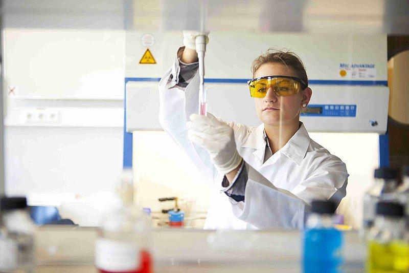 Person in a lab coat pipetting liquid in a laboratory.