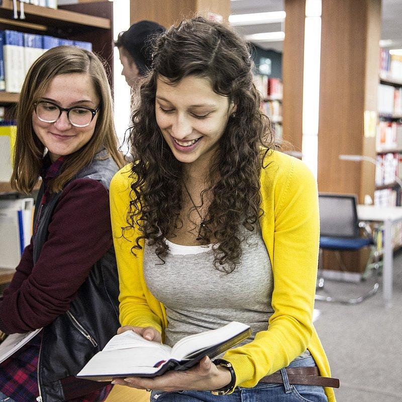Two people reading a book together in a library.