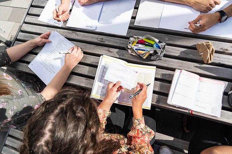 Nahaufnahme mehrerer Hände beim Schreiben in Notizbüchern.