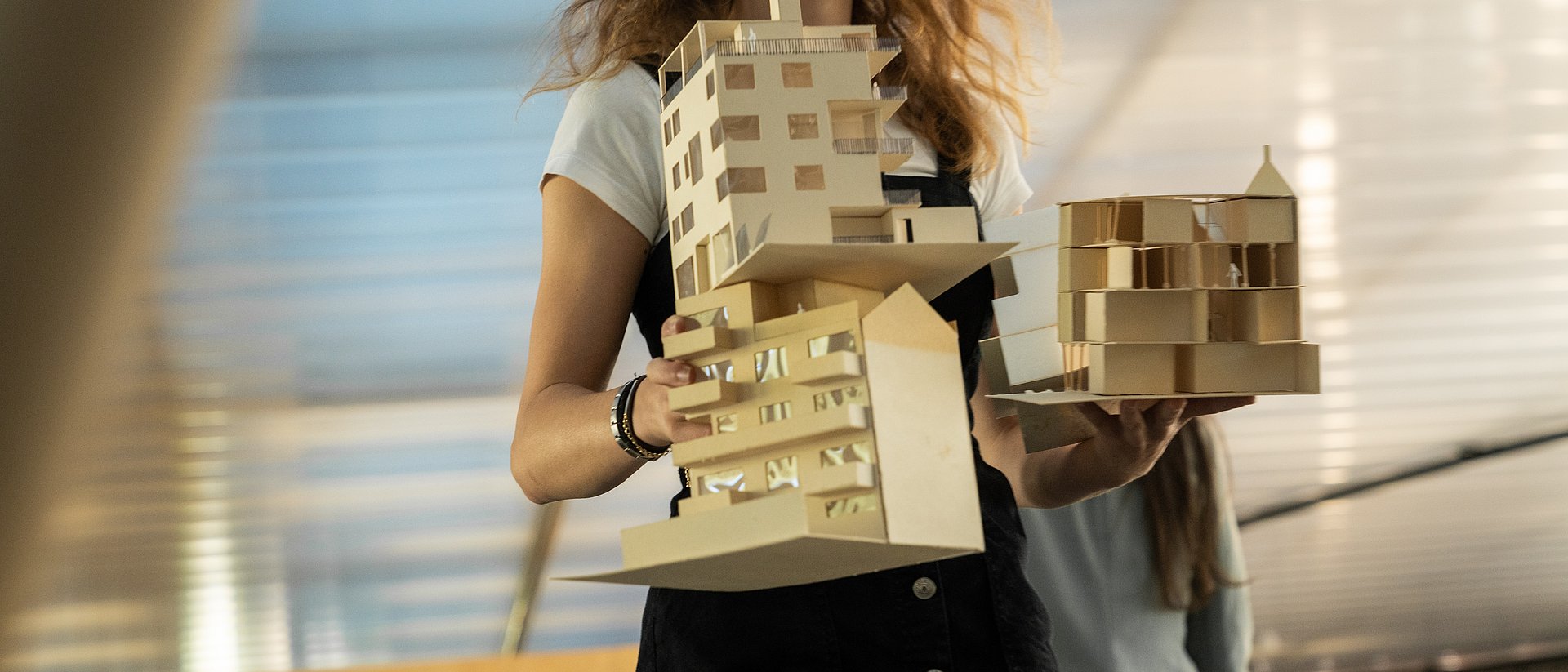 Person hält zwei Architekturmodelle aus Holz.