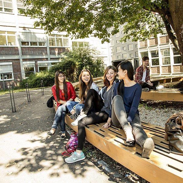 Several people sitting and laughing on benches under a tree in the courtyard.