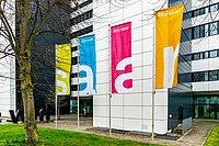 Vier bunte Fahnen mit „htw saar“ vor einem Gebäude.