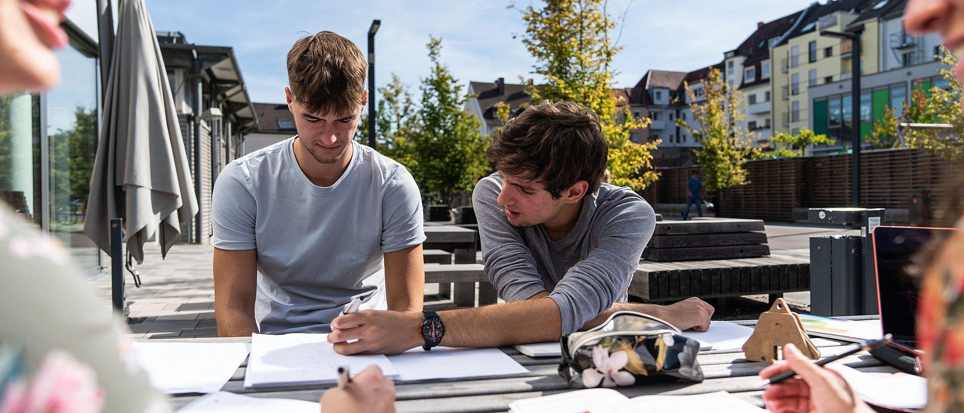 Gruppe von Studierenden arbeitet draußen an einem Tisch mit Unterlagen.