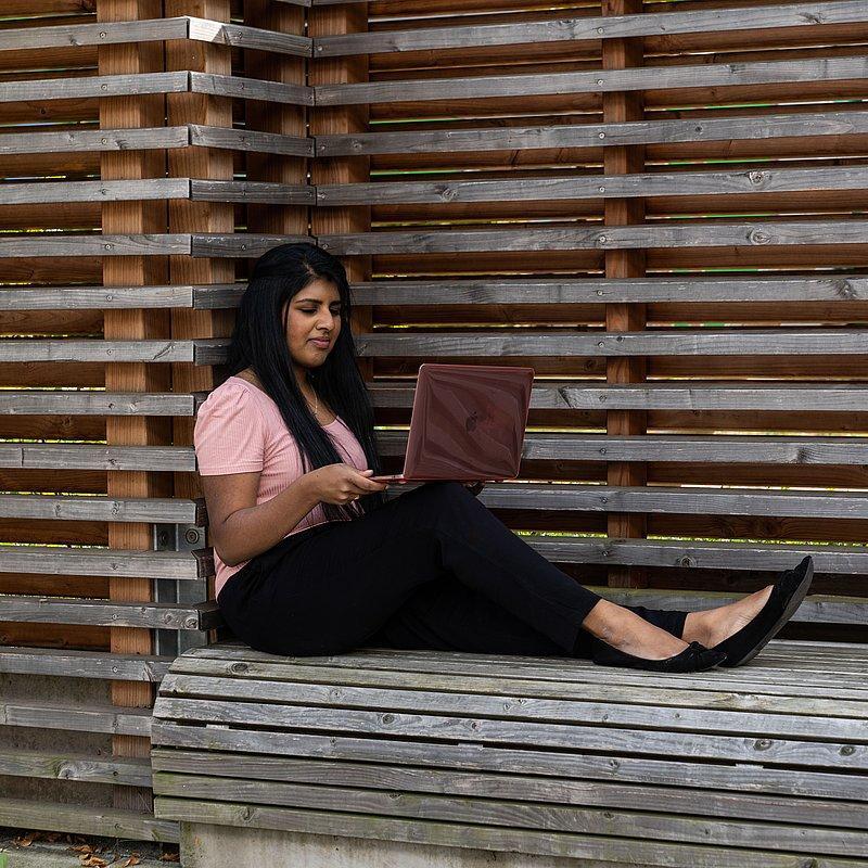 Person sitting on a wooden bench working on a laptop.