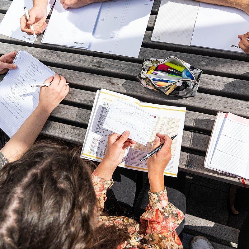 Close-up of several hands writing in notebooks.