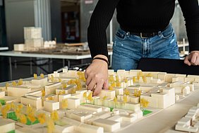 Hand platziert ein Element in einem Architekturmodell mit Bäumen.