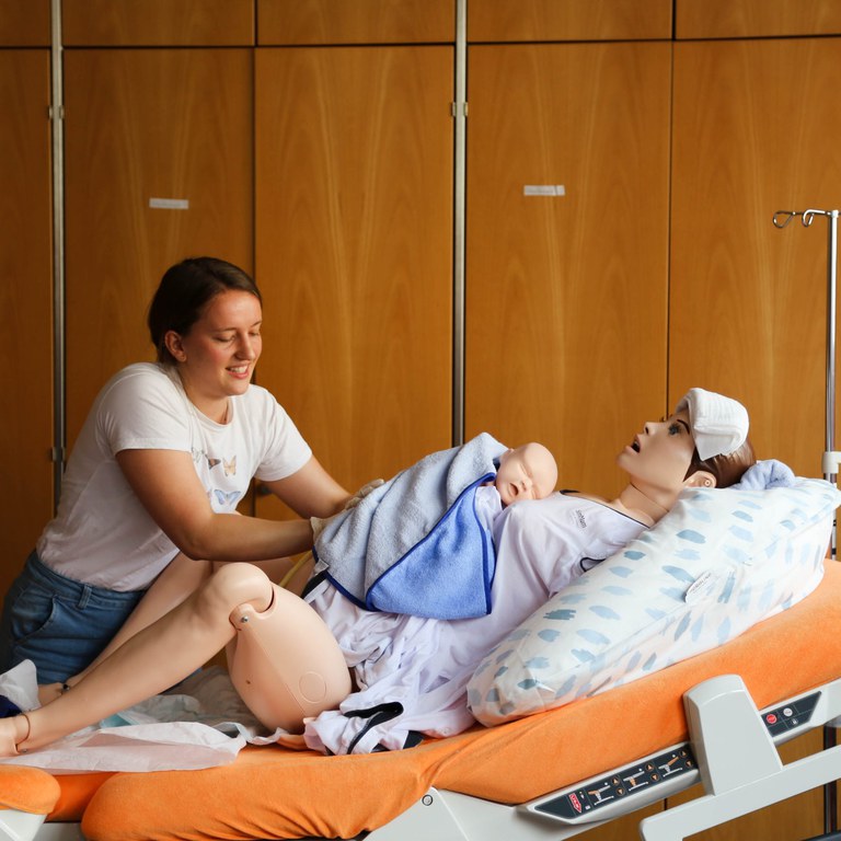 Person übt an einer Krankenpflegepuppe mit Baby im Krankenhausbett.
