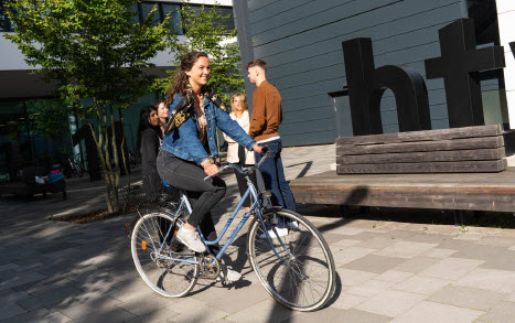 eine junge Frau fährt mit dem Fahrrad über den Hof vor dem Logo der htw saar