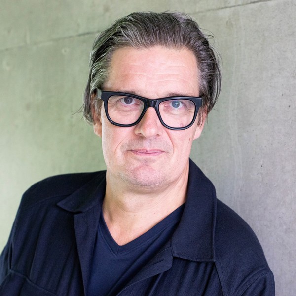 Das Foto zeigt Prof. Dipl.-Ing. Jens Metz, Professur für Städtebau, Transformation und Entwerfen an der htw saar. Er ist von der Brust aufwärts zu sehen, blickt geradeaus und lächelt nur leicht.  Er hat hellen Teint, mittellanges, nach hinten gekämmtes dunkelbraunes bis graumeliertes Haar und trägt eine auffällige schwarze Brille mit dicken Rahmen.   Er hat ein ovales Gesicht mit einigen leichten Falten an Stirn und um den Mund.   Er trägt ein dunkles T‑Shirt mit V‑Ausschnitt und darüber eine dunkle Jacke mit Kragen. 
