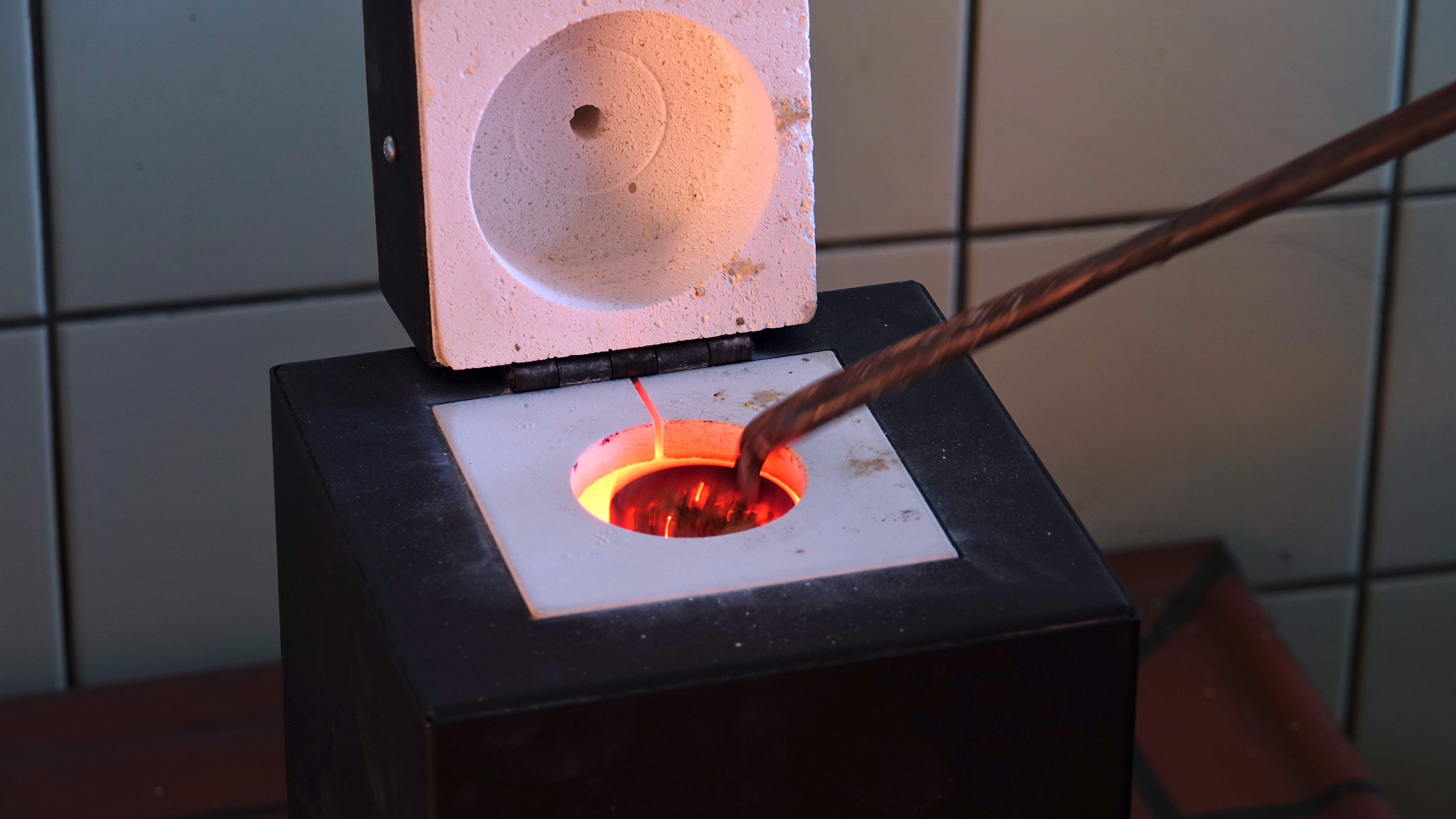 Tiegelschmelzofen nach oben geöffnet, glüht im Innern, mit Zange