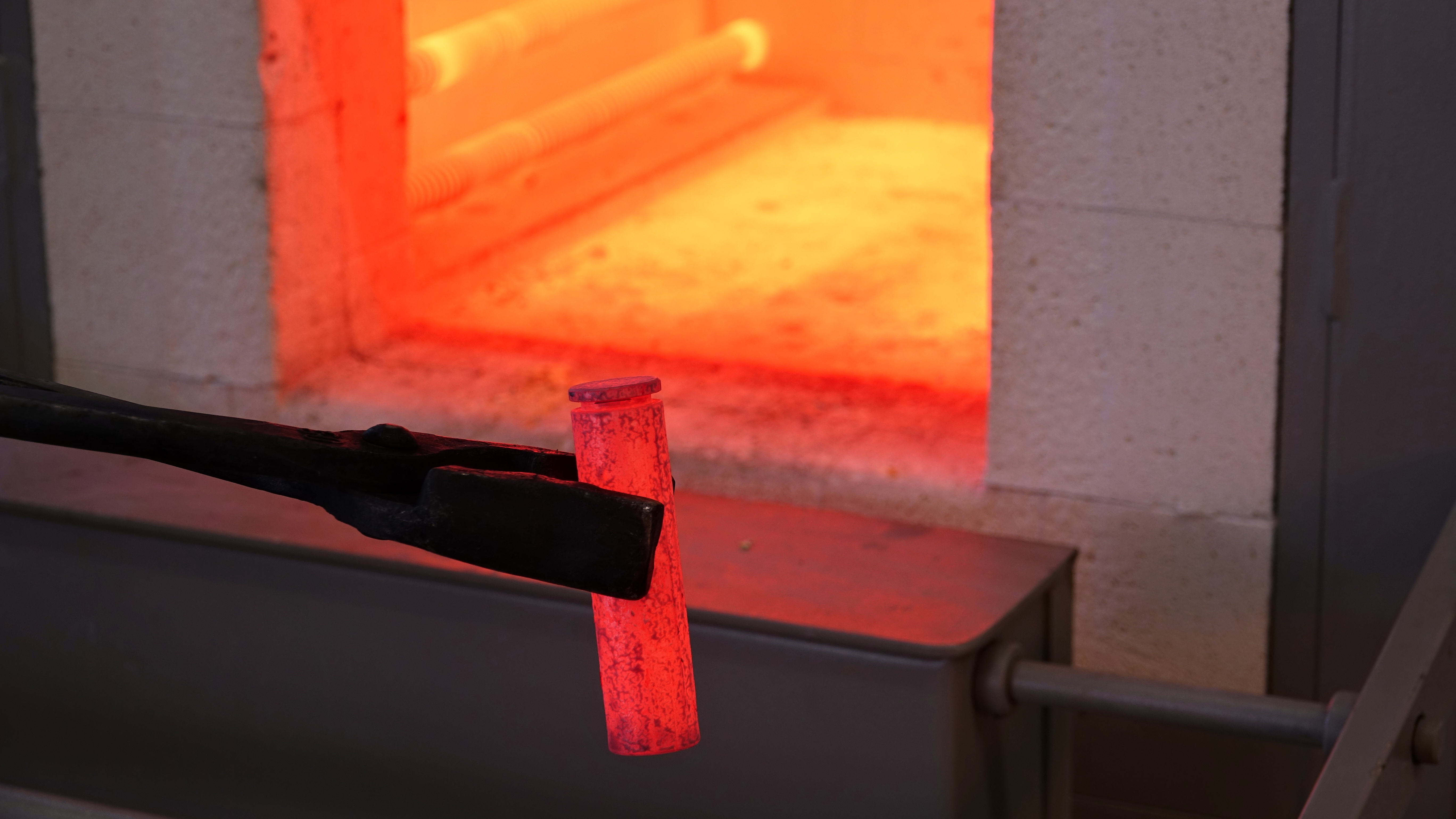 Geöffneter Kammerofen, glüht im Innern, davor Zange mit glühender Metallprobe